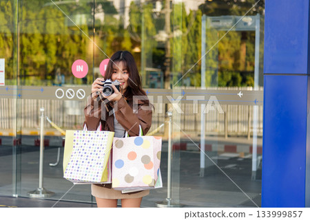 Asian woman shopping for fashion, bags, enjoying lifestyle, people shop at city mall, preparing for black friday, capturing moments with retro camera. 133999857