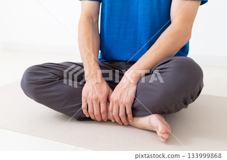 A middle-aged man wearing a T-shirt sitting cross-legged 133999868