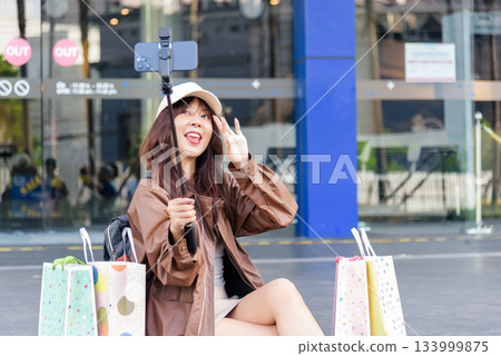Asian woman shopping, happy fashion lifestyle woman with bags near mall, people anticipating black friday deals, recording moment with phone. Asian woman shopping, happy fashion lifestyle woman with bags near mall, people anticipating black friday deals, recording moment with phone. 133999875