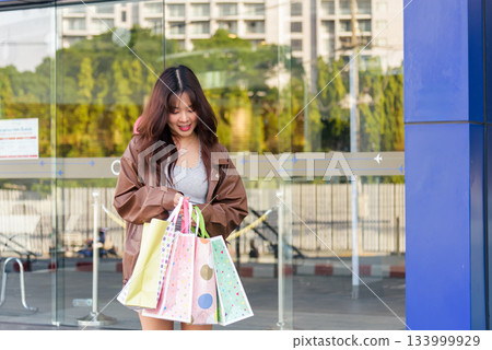 Asian woman shopping with fashion bags, people enjoy busy mall lifestyle, showing new purchases after exciting urban spree outside commercial district on black friday. 133999929