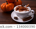 Pumpkin Spice Latte pumpkin drink topped with whipped cream sits in a white cup. Surrounding it pumpkins and cinnamon sticks creating a festive fall atmosphere. Pumpkin Spice Latte pumpkin drink topped with whipped cream sits in a white cup. Surrounding it pumpkins and cinnamon sticks creating a festive fall atmosphere. 134000390