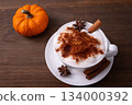 Pumpkin Spice Latte pumpkin drink topped with whipped cream sits in a white cup. Surrounding it pumpkins and cinnamon sticks creating a festive fall atmosphere. Pumpkin Spice Latte pumpkin drink topped with whipped cream sits in a white cup. Surrounding it pumpkins and cinnamon sticks creating a festive fall atmosphere. 134000392