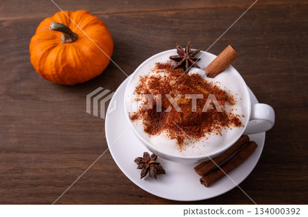 Pumpkin Spice Latte pumpkin drink topped with whipped cream sits in a white cup. Surrounding it pumpkins and cinnamon sticks creating a festive fall atmosphere. Pumpkin Spice Latte pumpkin drink topped with whipped cream sits in a white cup. Surrounding it pumpkins and cinnamon sticks creating a festive fall atmosphere. 134000392