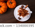 Pumpkin Spice Latte pumpkin drink topped with whipped cream sits in a white cup. Surrounding it pumpkins and cinnamon sticks creating a festive fall atmosphere. Pumpkin Spice Latte pumpkin drink topped with whipped cream sits in a white cup. Surrounding it pumpkins and cinnamon sticks creating a festive fall atmosphere. 134000395