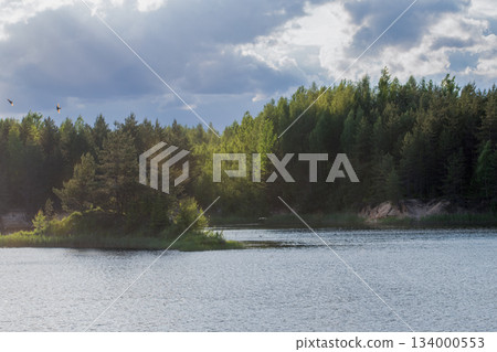 Serene landscape featuring a tranquil lake surrounded by lush green forests under a dramatic sky. Perfect for nature lovers and outdoor enthusiasts Serene landscape featuring a tranquil lake surrounded by lush green forests under a dramatic sky. Perfect for nature lovers and outdoor enthusiasts 134000553
