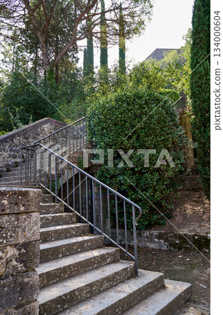 An old stone staircase leads upward through lush greenery in Gerona, Spain 134000604