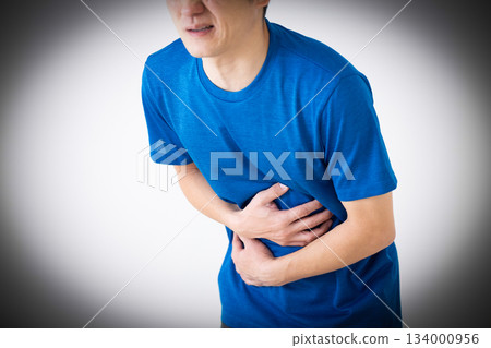 A middle-aged man wearing a T-shirt suffering from stomach pain 134000956