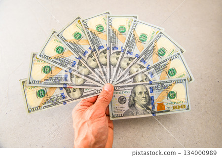 十張面值100美元的鈔票呈扇形展開，由左手拿著，清晰可見。 134000989