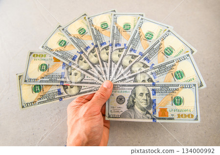 Ten US $100 bills fanned out and presented in the left hand (slightly blurred) 134000992