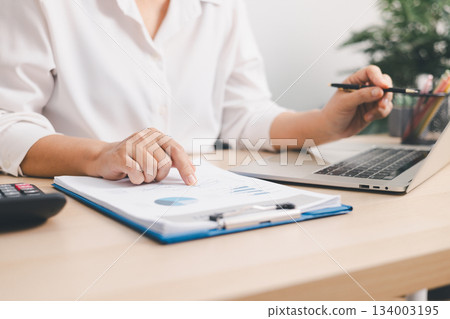 Close up of businessperson analyzing financial chart and graph with pen and calculator on desk, concept of accounting management, budget planning, financial report and data analysis. Close up of businessperson analyzing financial chart and graph with pen and calculator on desk, concept of accounting management, budget planning, financial report and data analysis. 134003195