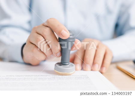 Businessperson stamping document on clipboard at office desk, concept of contract approval, legal authorization, business agreement validation or administrative paperwork process. stamp approval. Businessperson stamping document on clipboard at office desk, concept of contract approval, legal authorization, business agreement validation or administrative paperwork process. stamp approval. 134003197