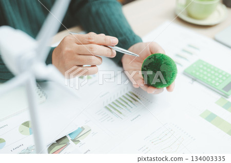 Eco-friendly business concept with hand analyzing financial charts and green earth globe symbolizing sustainable investment, environmental data analysis and green economy growth. green business. 134003335
