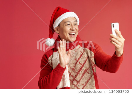 Man Wearing a Santa Hat Takes a Joyful Selfie During the Holiday Season Against a Red Backdrop in a Festive Setting 134003700