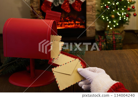 Letters to Santa. Santa's hand placing letters in a red mailbox by a cozy fireplace 134004240