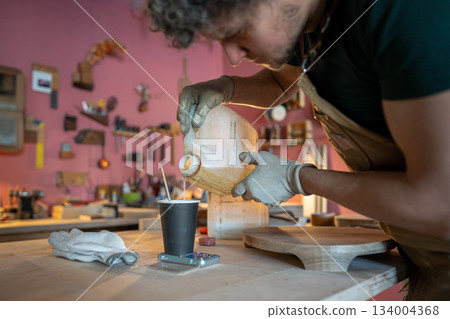 Man carpenter preparing for work, measuring required amount of epoxy resin on a scale at table. Man carpenter preparing for work, measuring required amount of epoxy resin on a scale at table. 134004368