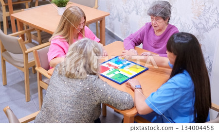 Women playing board game in nursing home with caregiver 134004458