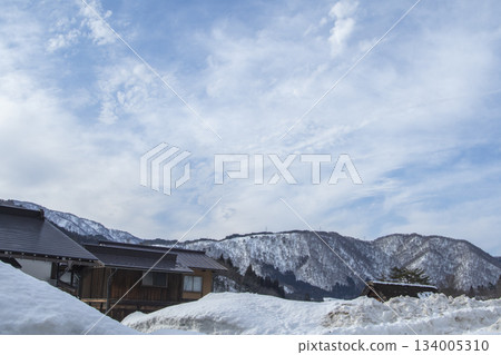 一幅展現日本山村民居風貌的風景畫，背景是廣闊的雪原和皚皚雪山。 134005310