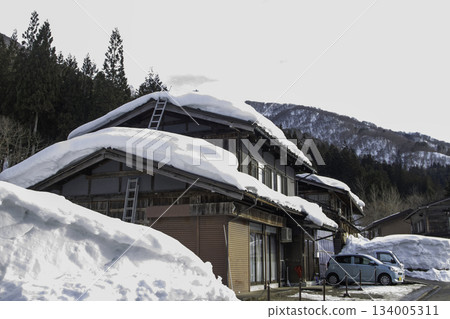 一架梯子懸掛在被雪覆蓋的房屋屋頂上。 一架梯子懸掛在被雪覆蓋的房屋屋頂上。 134005311