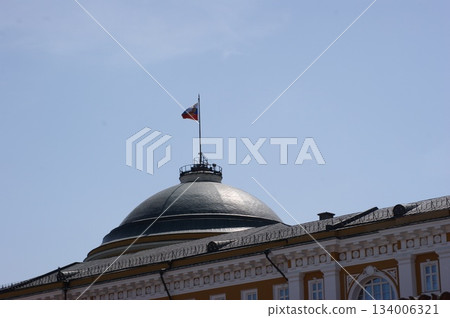 The photograph shows part of a building with a dome and a flag on top. The building has classical architecture with white and orange elements. The flag displays the colors of the Russian flag: white, The photograph shows part of a building with a dome and a flag on top. The building has classical architecture with white and orange elements. The flag displays the colors of the Russian flag: white, 134006321