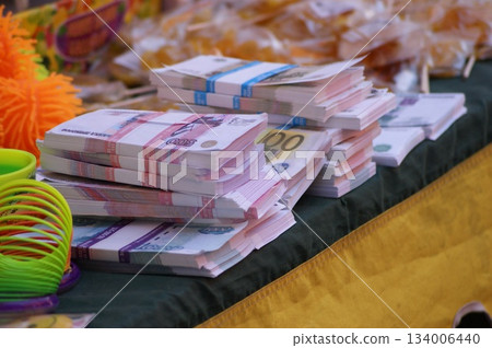 The photograph shows stacks of money neatly arranged on a table. The money is of various denominations, including 100- and 500-euro bills. Colorful jewelry and other objects are visible in the backgro The photograph shows stacks of money neatly arranged on a table. The money is of various denominations, including 100- and 500-euro bills. Colorful jewelry and other objects are visible in the backgro 134006440