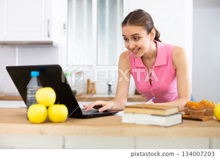 Emotional woman using laptop for work or study in home kitchen Emotional woman using laptop for work or study in home kitchen 134007203