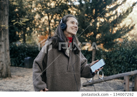 Young Woman Enjoying Music in Park During Autumn Young Woman Enjoying Music in Park During Autumn 134007292