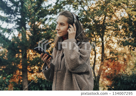 Young Woman Enjoying Music in Park During Autumn 134007295