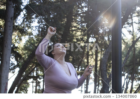 an adult woman doing stretching exercises outside in green park, mental setting training 134007860