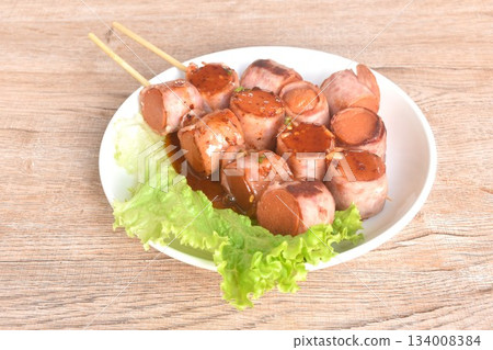 pork sausage roll up bacon stabbing plant stick dressing spicy barbecue sauce arranging with vegetable on plate pork sausage roll up bacon stabbing plant stick dressing spicy barbecue sauce arranging with vegetable on plate 134008384