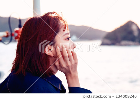 The back view of a woman in her twenties gazing at the sea at sunset 134009246