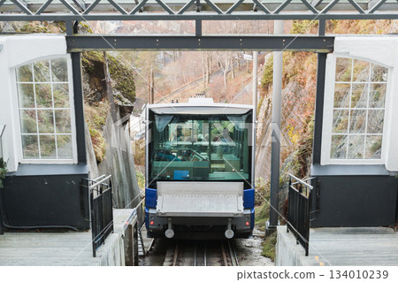 A modern cable car enters a glass-walled station, passengers visible inside 134010239