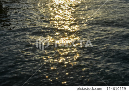 Reflection of golden sunlight on water. Sunset sea view with sparkle sunlight. Sunset light hitting on the ocean. Sunset sea background. 134010359