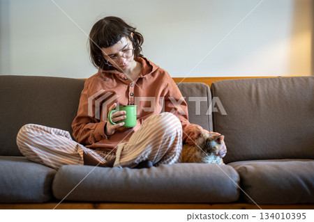 Loving teenager spending time at home with beloved cat Devon Rex, sitting on couch, drinking tea 134010395