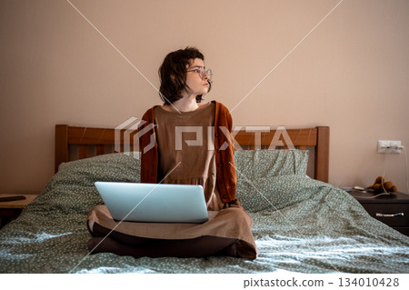 Tired teen girl sitting on bed, having break after long freelance work, hard online studying 134010428