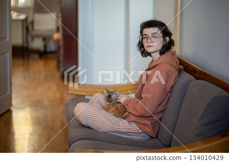 Brooding teenager, pet owner sitting on couch, thinking, stroking sleepy breed cat lying on knees 134010429