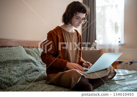 Concentrated pensive teen girl working as freelancer, studying online at home using laptop computer 134010493