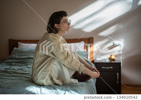 Melancholic teen girl sitting on bed in apathetical, depressed mood, thinking of misunderstanding Melancholic teen girl sitting on bed in apathetical, depressed mood, thinking of misunderstanding 134010542
