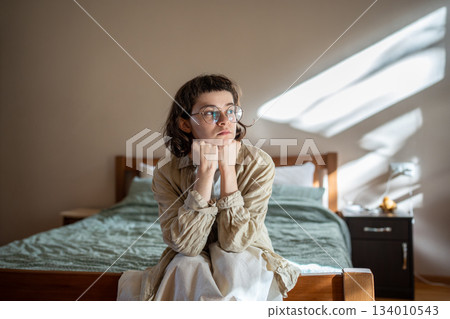 Depressed lonely young woman sitting on cozy bed sadly looking at window feeling anxiety, sorrow. Depressed lonely young woman sitting on cozy bed sadly looking at window feeling anxiety, sorrow. 134010543