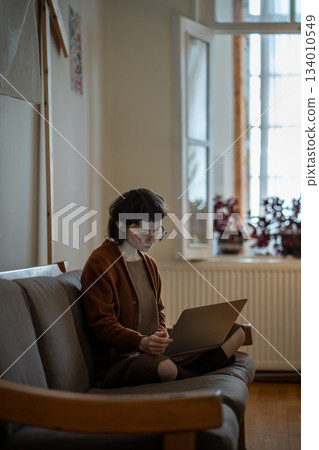 Focused teen girl working on laptop, using social media sitting on couch at home. Freelance Focused teen girl working on laptop, using social media sitting on couch at home. Freelance 134010549