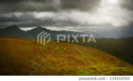 Moody clouds casting shadows over the rugged terrain. 134010584