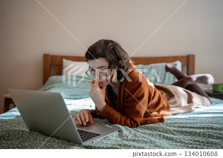 Concentrated teen girl reading book online, scrolling social networks in internet on laptop computer Concentrated teen girl reading book online, scrolling social networks in internet on laptop computer 134010608