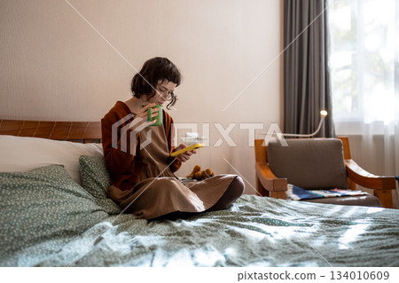 Pensive woman sitting on bed with cup of tea, reading news in internet, hanging in social network 134010609