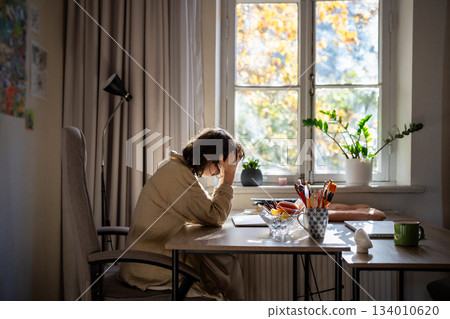 Stressed woman with burnout sits at table holding head with hands feeling bad having, work problem Stressed woman with burnout sits at table holding head with hands feeling bad having, work problem 134010620