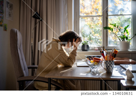 Tired exhausted woman sitting at table holding head early morning after working all night. Tired exhausted woman sitting at table holding head early morning after working all night. 134010631