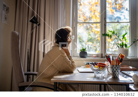 Woman painter having inspiration to create new picture sitting at desk thinking looking at window. Woman painter having inspiration to create new picture sitting at desk thinking looking at window. 134010632