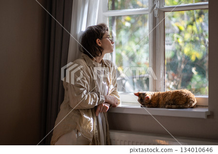 Melancholic pet owner looking at window in depression while staying at home in sunny summer day Melancholic pet owner looking at window in depression while staying at home in sunny summer day 134010646