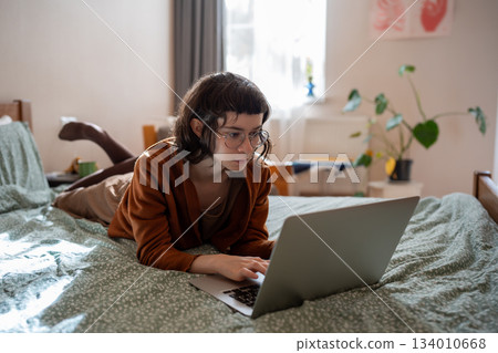 Student girl nerd in glasses studying on laptop at home lying in bed. Distant education, homework Student girl nerd in glasses studying on laptop at home lying in bed. Distant education, homework 134010668