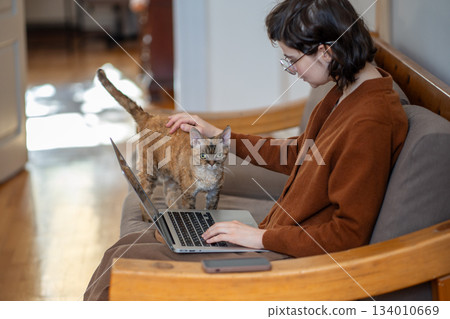 Tender loving girl sitting on couch, stroking cat who diverts girl attention from work, study Tender loving girl sitting on couch, stroking cat who diverts girl attention from work, study 134010669