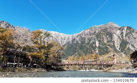 Spectacular views of Kappa Bridge and the Hotaka mountain range | Kamikochi: Bustling Kappa Bridge in autumn | Tourists passing by, autumn leaves and snow-capped mountains 134010679