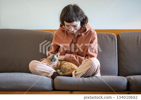 Loving pet owner sitting on couch, holding cat on knees, looking at kitty with love and tenderness Loving pet owner sitting on couch, holding cat on knees, looking at kitty with love and tenderness 134010682